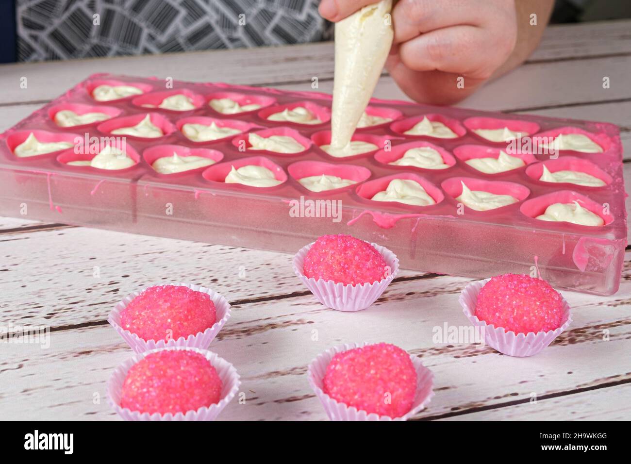 Bicho de pe, brasilianische Süßigkeiten. Im Hintergrund ein Bäcker, der Bonbons mit Ganache füllt. Stockfoto