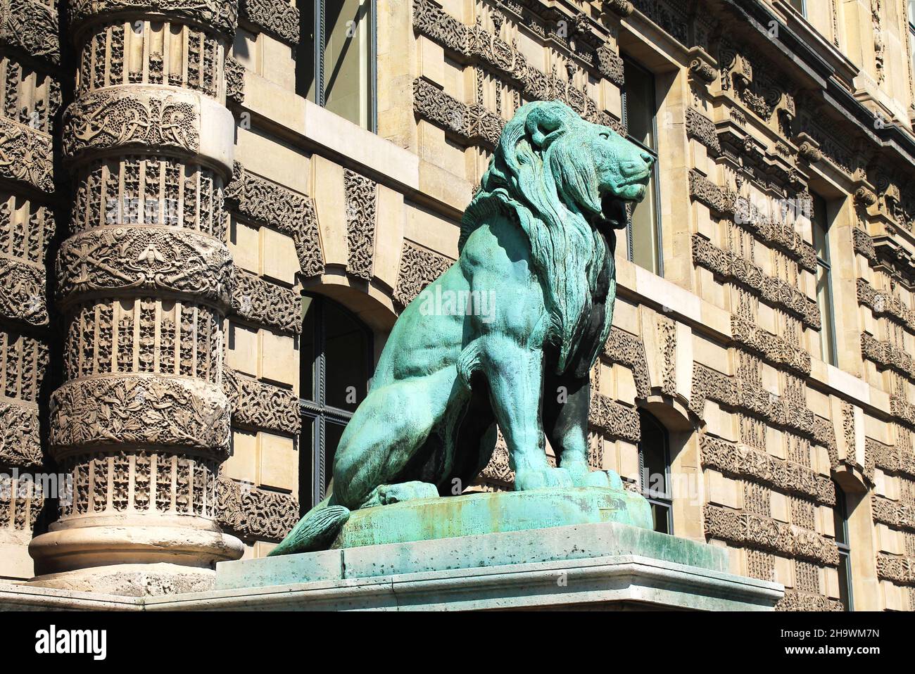 Bronzelöwenskulptur mit verwitterter grüner Verdigris patina steht an einem sonnigen Tag am Porte des Lions vor dem Louvre in Paris, Frankreich. Stockfoto
