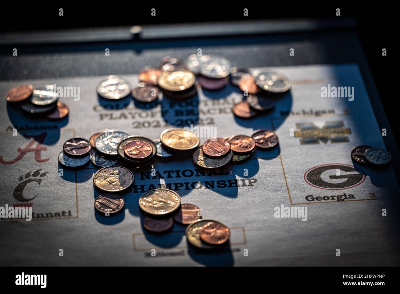 Tiffin, Iowa, USA - 12,2022 - Selektiver Fokus auf 2021-2022 College Football Playoff Bracket mit verstreuten Münzen. Stockfoto