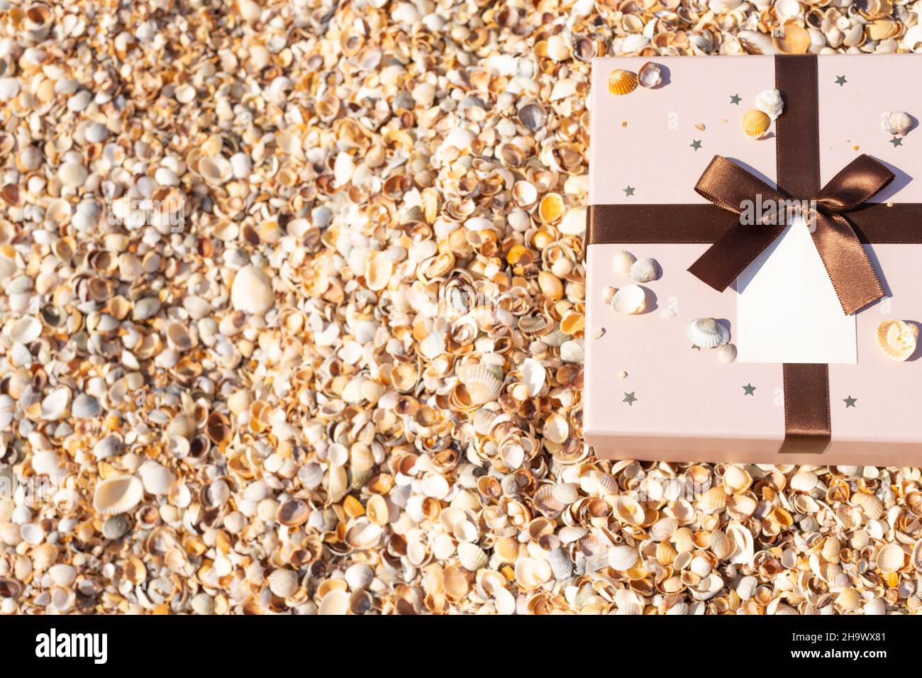 Am Strand in der Nähe des Meeres liegt eine Schachtel mit einem mit einem Band gebundenen Geschenk. Vorderansicht, vertikal. Stockfoto