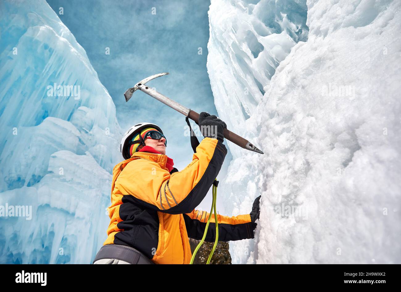 Die Frau klettert in den Bergen mit Eispickel in orangefarbener Jacke über einen gefrorenen Wasserfall. Sportbergsteigen und Alpinismus Konzept. Stockfoto