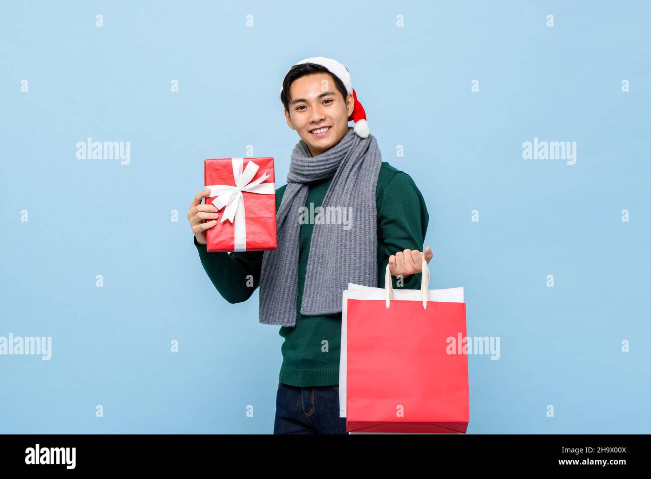 Glücklich asiatischen Mann hält Weihnachten Geschenkbox und shoppen Taschen In hellblauem Studio isolierten Hintergrund Stockfoto