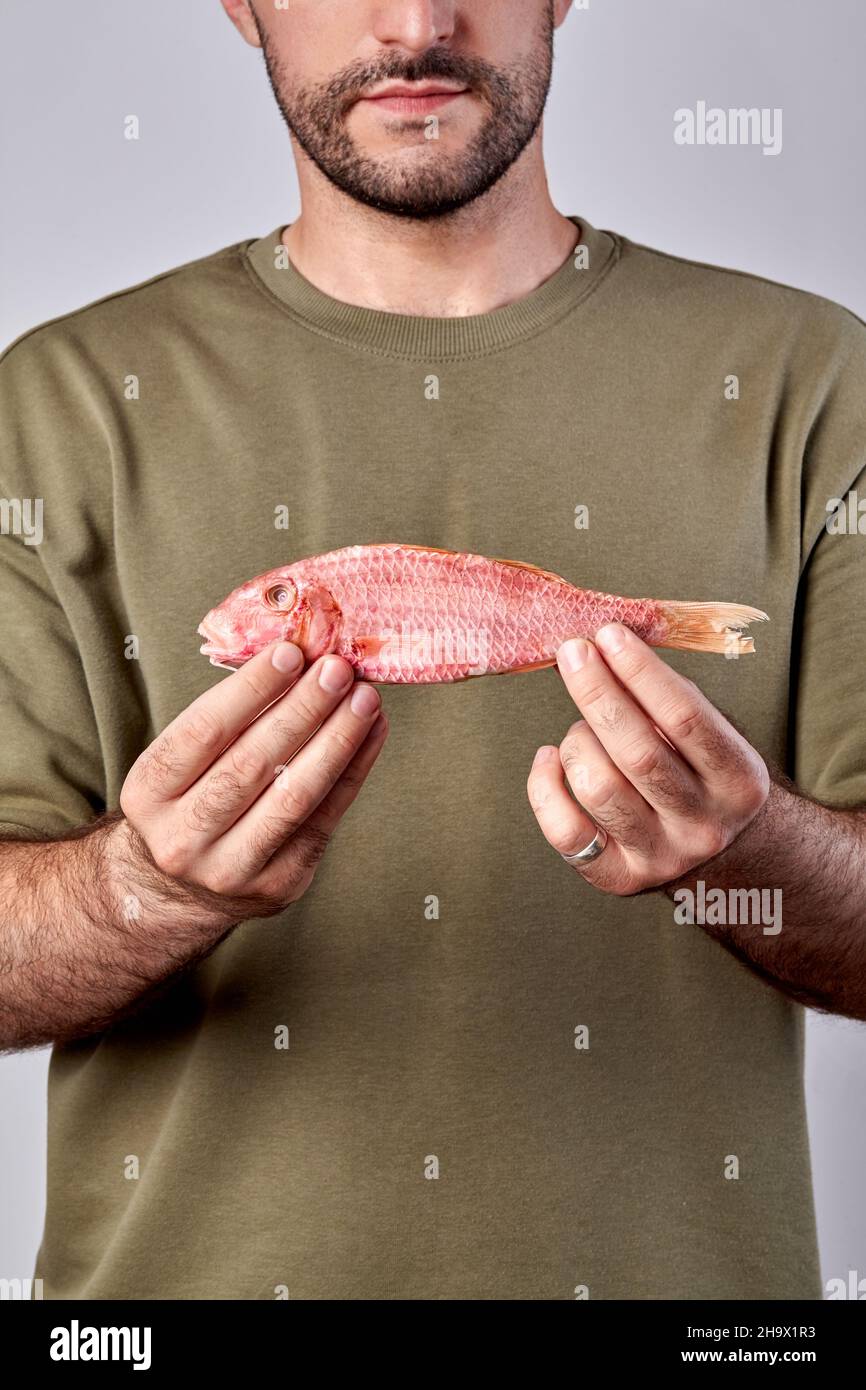 Bärtiger Mann, der eine getrocknete, gesalzene rote Meerbarbe in den Händen hält Stockfoto