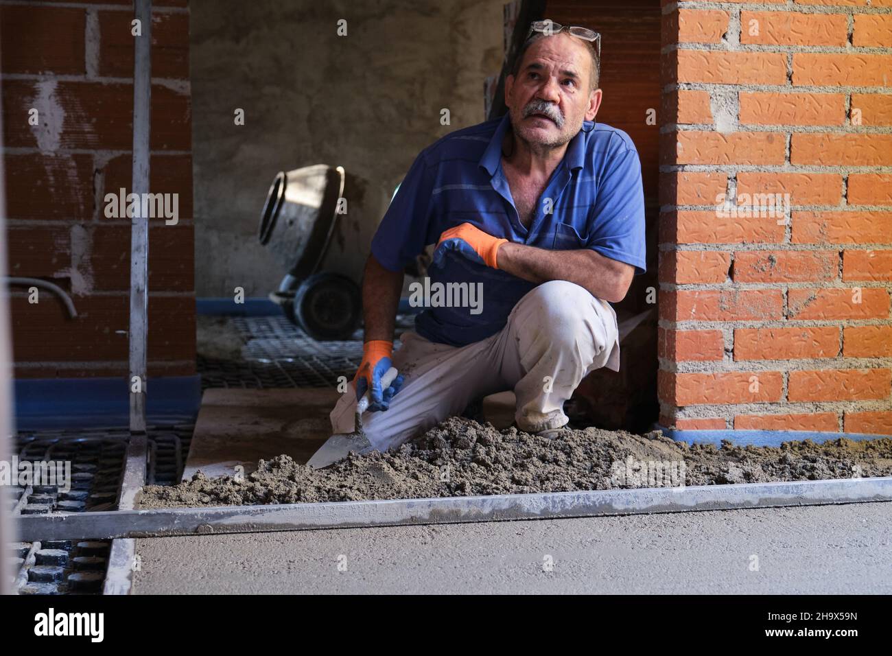 Der Baumeister hört seinem Chef zu, während er Beton über dem strahlenden Boden verteilt. Stockfoto