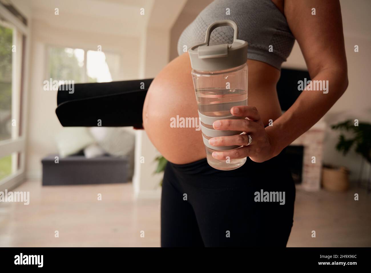 Kaukasische Frau, die im Wohnzimmer mit Wasserflasche und Yogamatte steht Stockfoto