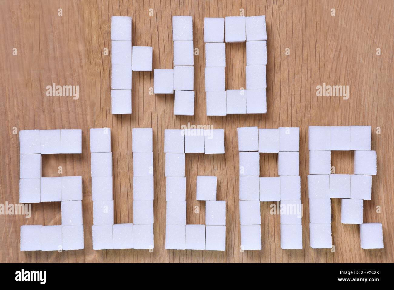 Die Worte NO SUGAR, ausgekleidet mit Würfeln raffinierten Zuckers auf braunem Holzgrund, sind verboten. Nahaufnahme Stockfoto
