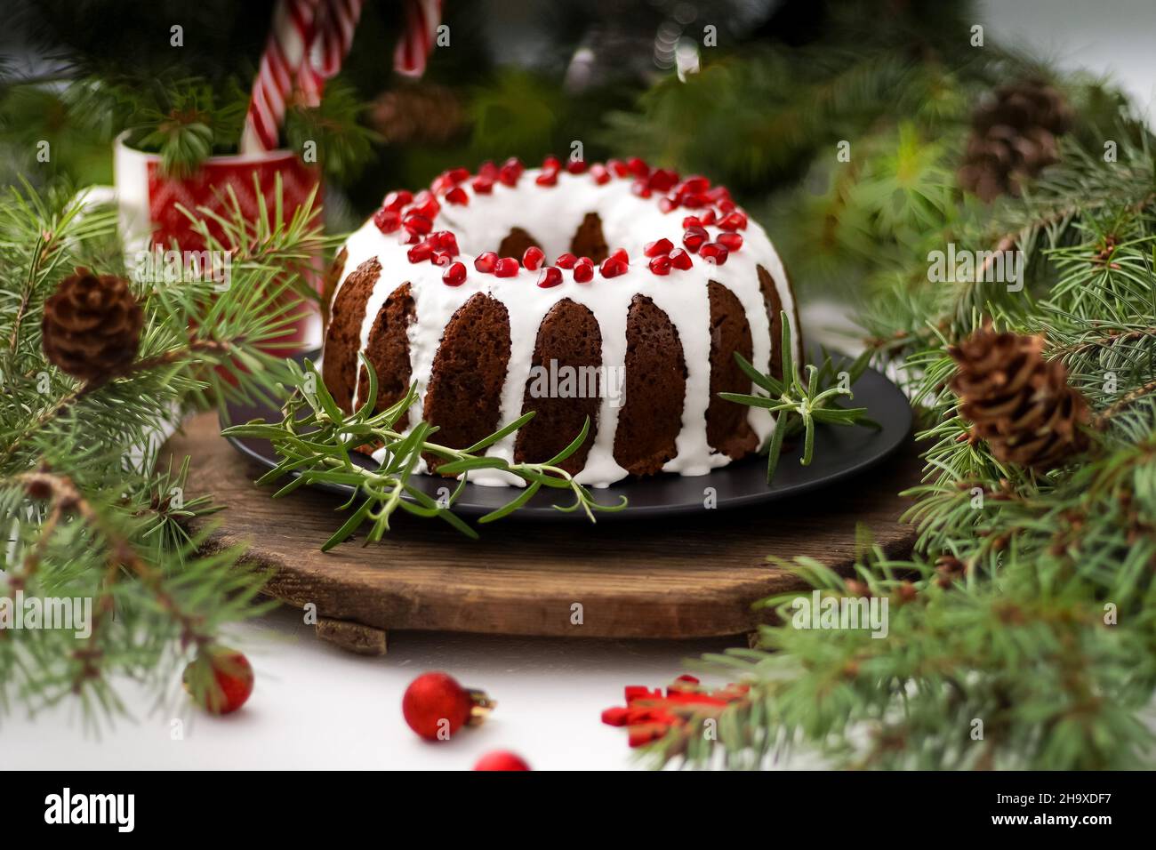 Weihnachtliches Essen. Runde Torte mit weißer Glasur. Cupcake mit einem Loch in der Mitte mit Granatapfel. Grüne Fichtenzweige auf dem Tisch. Stillleben. Süßes Gebäck, Desserts und Leckereien für das neue Jahr. Stockfoto