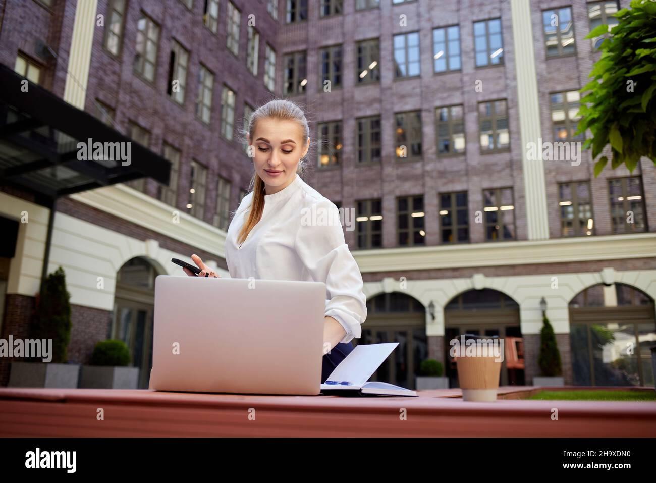 Erfolgreiche Geschäftsfrau mit Smartphone, das an einem Laptop im Freien arbeitet. Stockfoto
