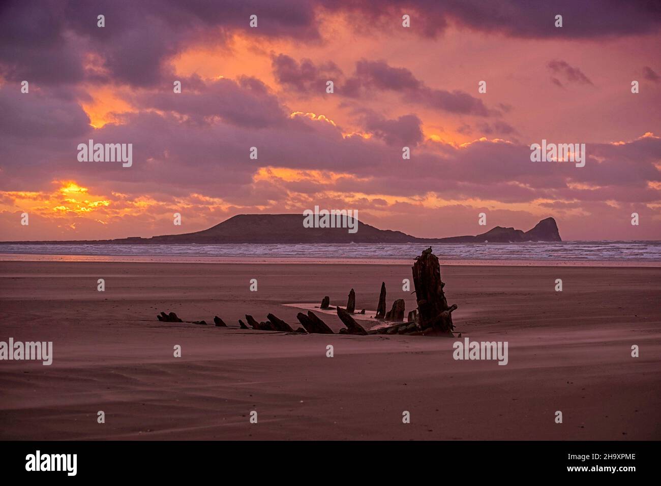 Der Himmel leuchtet rosa, als die Sonne hinter dem Schiffswrack der Helvetia aus dem Jahr 1887 am Rhossili Beach auf der Gower Peninsula in Südwales an diesem Abend untergeht Stockfoto