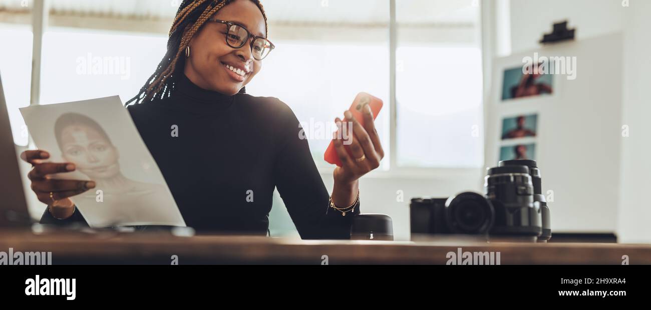 Kreative Künstlerin, die in ihrem Heimbüro einen Videoanruf entgegennimmt. Fröhliche junge Fotografin, die fröhlich lächelt, während sie mit ihren Kunden kommuniziert. Femal Stockfoto