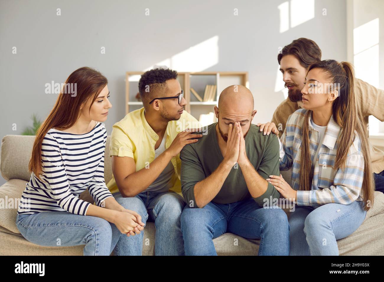 Unterstützende Gruppe von Menschen trösten ihren traurigen männlichen Freund, der seine Probleme mit Freunden teilt. Stockfoto