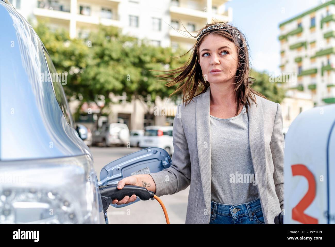 Frau lädt ein Elektroauto in städtischen Umgebungen, Faro, Portugal Stockfoto