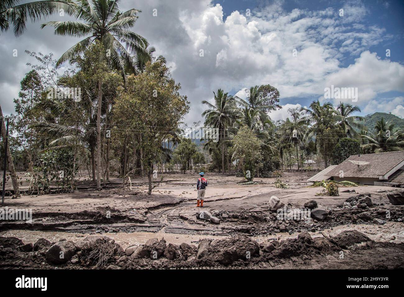 Kamar Kajang, Indonesien. 09th Dez 2021. Ein indonesischer Rettungsbeamter steht in der Nähe von Bäumen und einem mit Vulkanasche bedeckten Haus, während er in den Dörfern Kamar Kajang, Lumajang, nach Opfern sucht. Mindestens 14 Menschen sind tot und Dutzende werden verletzt, nachdem Mount Semeru, ein Vulkan in der indonesischen Provinz Ost-Java, am Samstag ausbrach und Aschetürme und heiße Wolken warf, die nahe gelegene Dörfer bedeckten. (Foto: Aditya Saputra/SOPA Images/Sipa USA) Quelle: SIPA USA/Alamy Live News Stockfoto