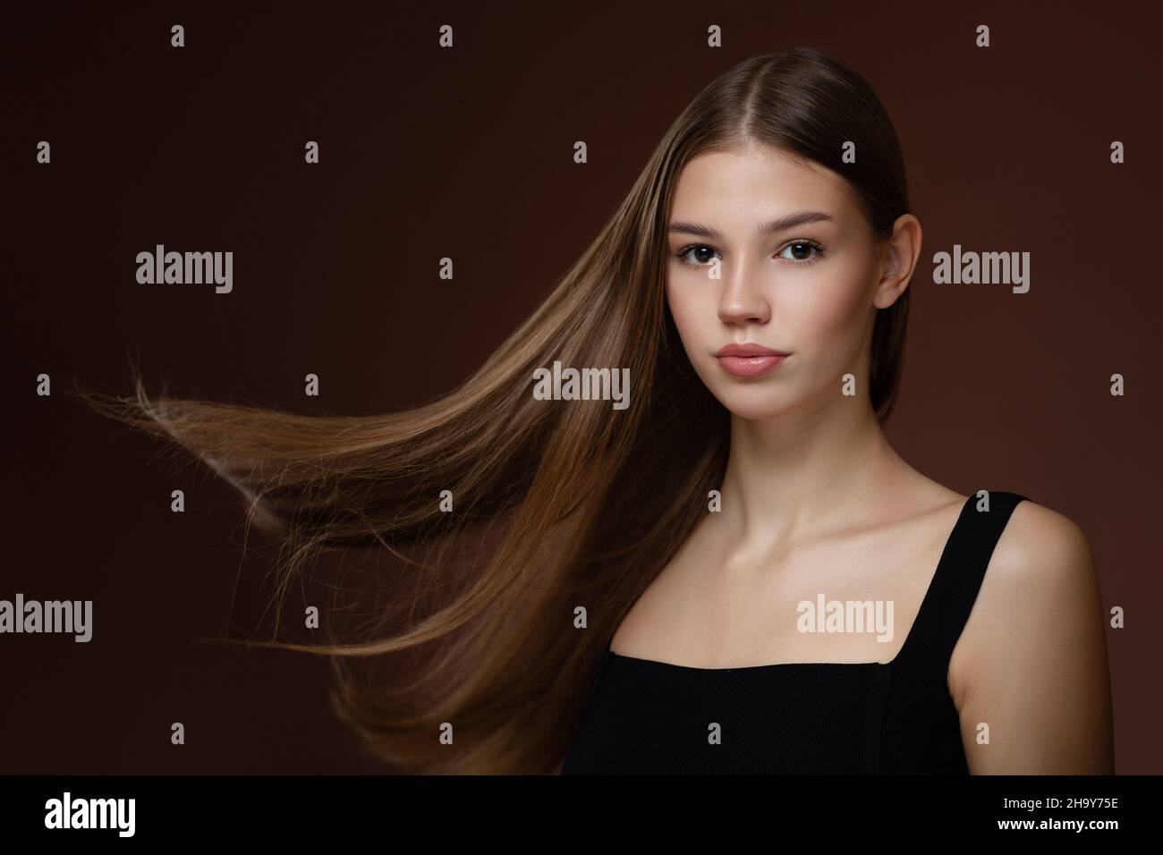 Schöne junge Frau mit langen geraden Haaren und Make-up. Brauner Hintergrund Stockfoto