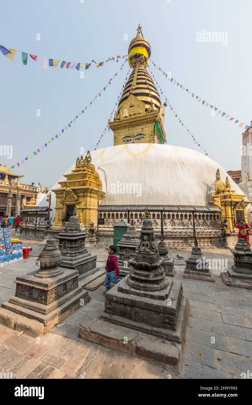 Ein kleiner Junge steht unter den Chaityas im Swayambhunath-Tempelkomplex in Kathmandu, Nepal. Der Hauptstupa ist dahinter. Stockfoto