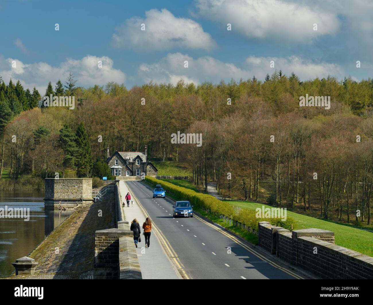 Sonnige, landschaftlich reizvolle Landschaft (Spaziergänger auf dem Bürgersteig, Autos auf der Straße, Ventilturm, Haus) - Fewston Reservoir, Washburn Valley, Yorkshire, England, Großbritannien. Stockfoto