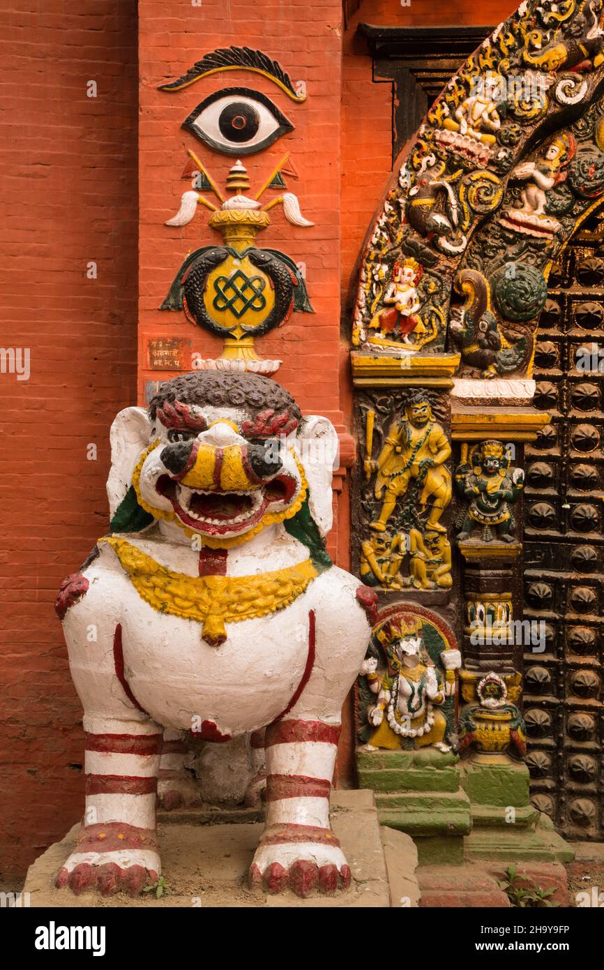 Eine steinerne weiße Löwenstatue bewacht das Singha Dhoka Gate, Durbar Square, Kathamandu, Nepal. Der Bogen um das Tor ist mit detaillierten Steinwagen bedeckt Stockfoto