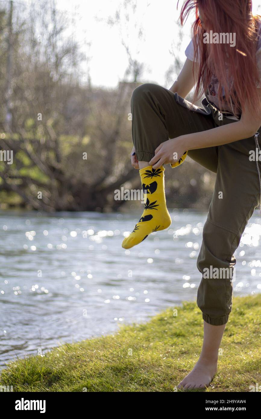 Vertikale Aufnahme einer jungen Frau, die am Flussufer die Socken auszieht Stockfoto