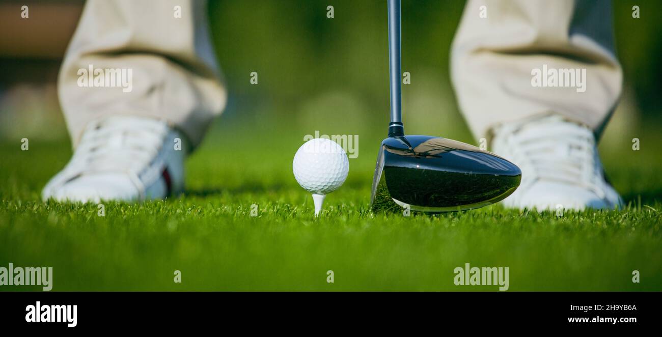 Golfball auf dem T-Shirt auf dem Turf Grass-Kurs, Golfschläger vom Golfclub-Fahrer. Weiße Golfschuhe Close-Up . Hochwertige Fotos Stockfoto