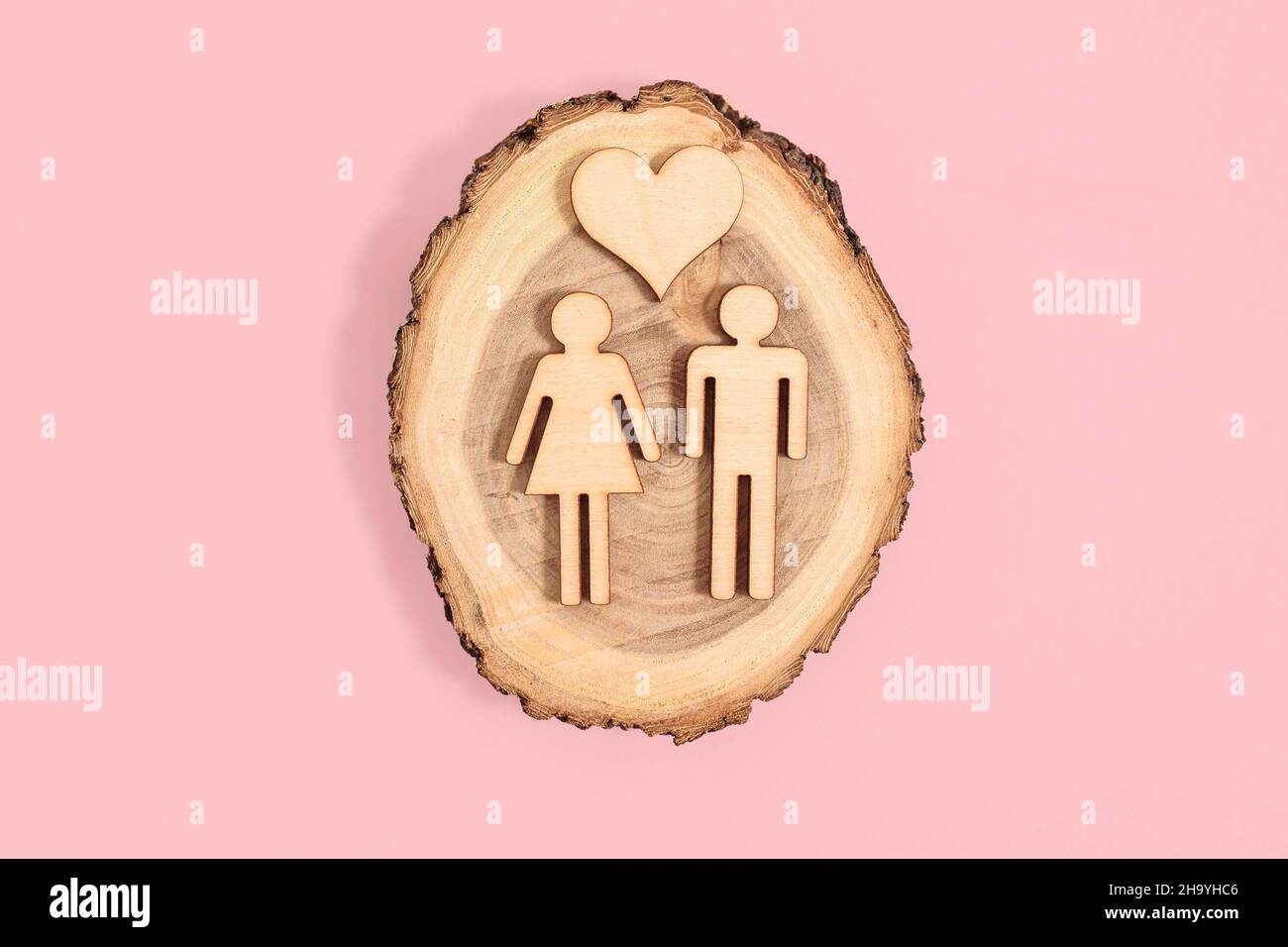 Holzfiguren von Mann und Frau und Herz auf rosa Hintergrund. Valentinskarte Stockfoto