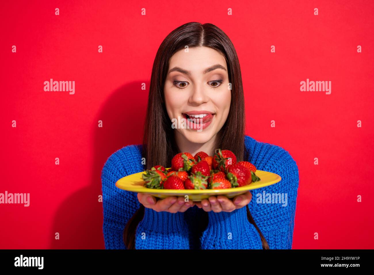 Foto von charmanten hungrigen jungen Frau halten Platte Erdbeere lecken Zungenzähne auf rotem Hintergrund isoliert Stockfoto