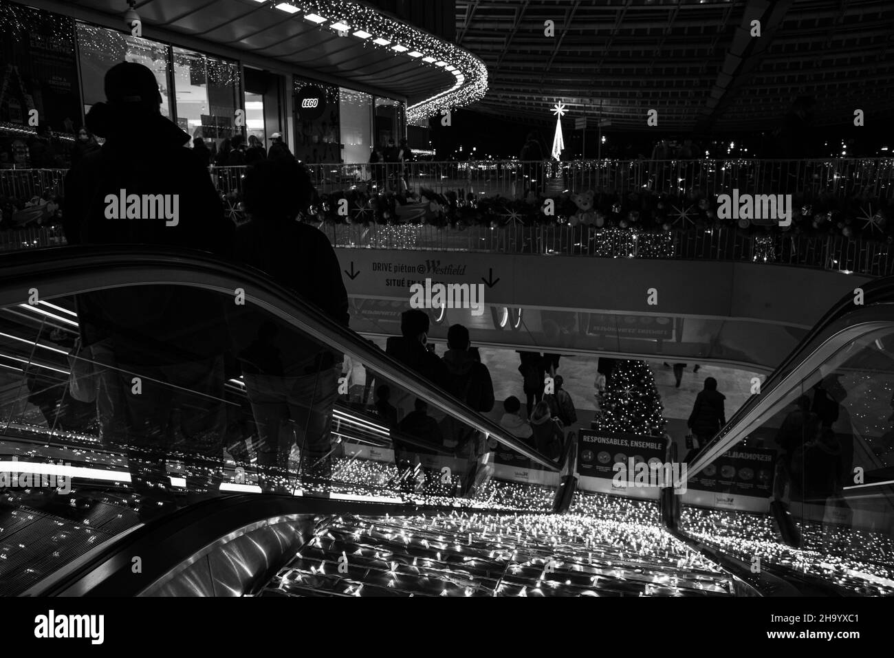 Paris, Frankreich - 18. Dezember 2021: Einkaufsbummel auf Rolltreppen im Einkaufszentrum Westfield Forum des Halles während der Winterurlaubsverkäufe. Schwarzweißfoto Stockfoto