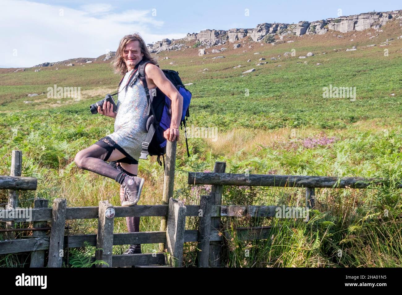 Derbyshire UK – 20. Aug 2020: Ein Mann in einem funkelnden Kleid und Strümpfen posiert auf einem Stil in der Hochmoorlandschaft des Distrikts Stanage Edge Stockfoto