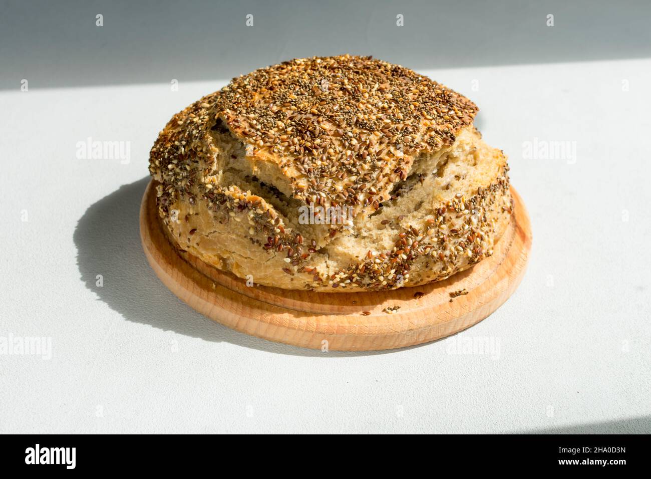 Natürliches Brot aus hefefreiem Sauerteig mit Sesamsamen, Flachs, Chia, Sonnenblumenkernen, auf einem Holzbrett auf dem Tisch, Nahaufnahme. Stockfoto