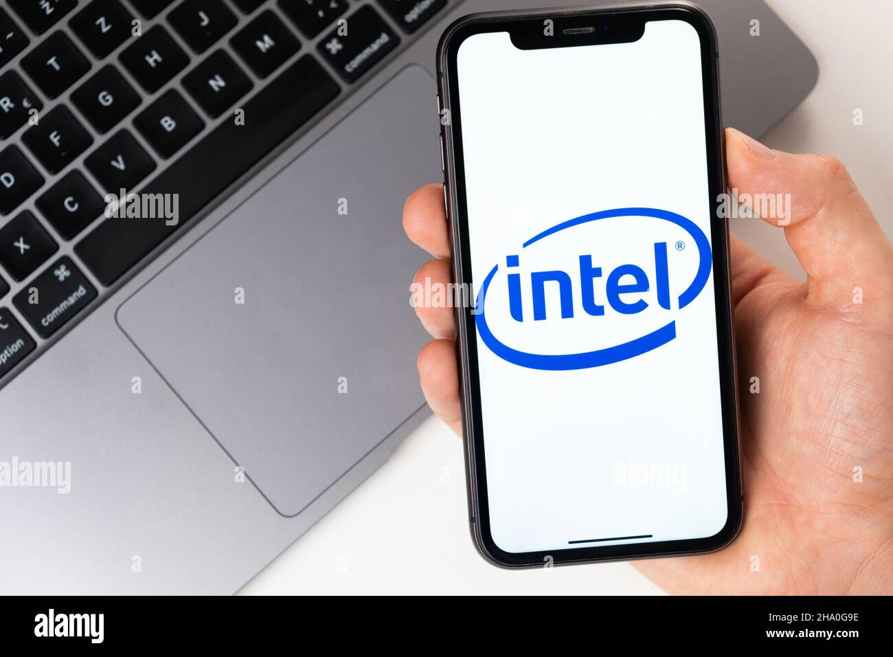 Intel Mobile-Anwendung auf dem Smartphone-Bildschirm. Ein Mobiltelefon in einer Männerhand in der Nähe eines offenen Laptops. Weißer Hintergrund. November 2021, San Francisco, USA Stockfoto