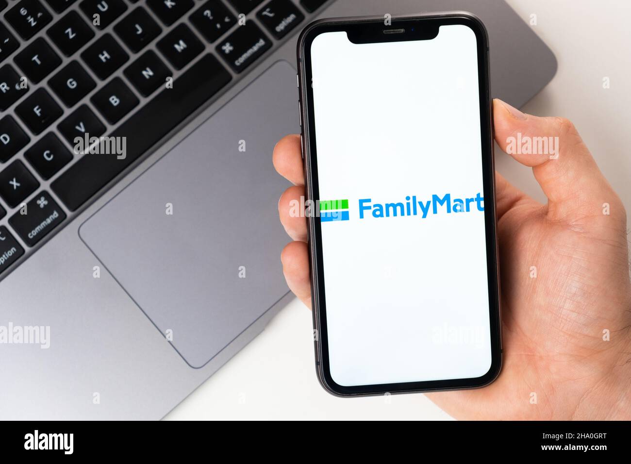 FamilyMart mobile Anwendung auf dem Smartphone-Bildschirm. Ein Mobiltelefon in einer Männerhand in der Nähe eines offenen Laptops. Weißer Hintergrund. November 2021, San Francisco, USA Stockfoto