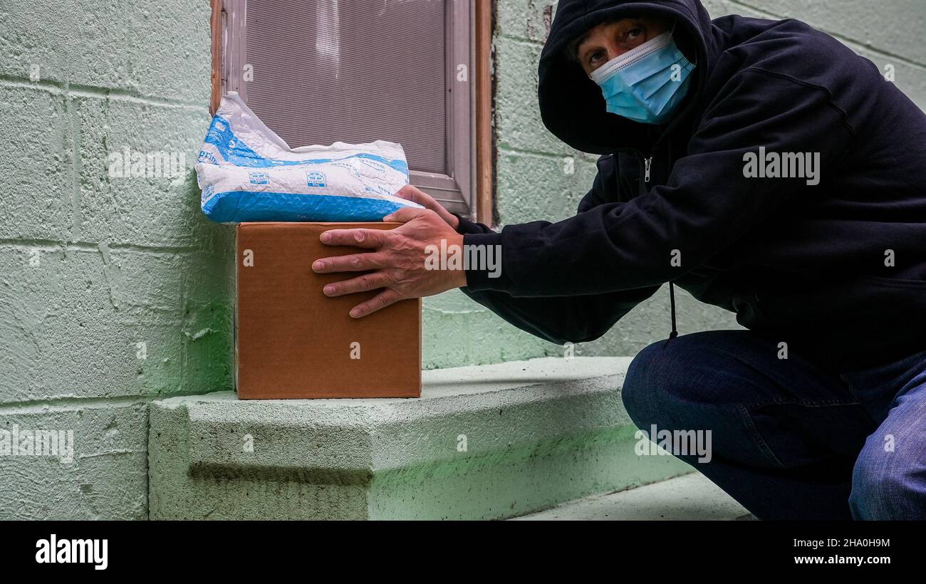 NORWALK, CT, USA - 8. DEZEMBER 2021: Konzeptfoto vom Mann, der Amazon-Paket gestohlen hat, mit einer anderen Box, die an die Haustür geliefert wurde Stockfoto