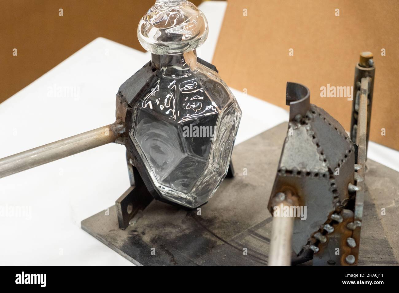 Stilvolle Glasflasche in offener Metallform auf der Werkbank in der Licht-Werkstatt in der traditionellen Glasbläserei extreme Nahsicht Stockfoto