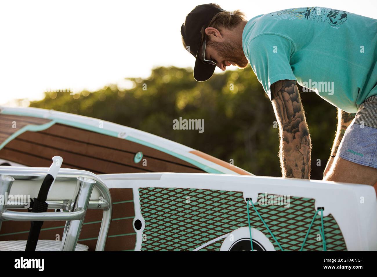 Ein Mann mit Tattoos lädt Paddle Boards auf dem Boot Stockfoto
