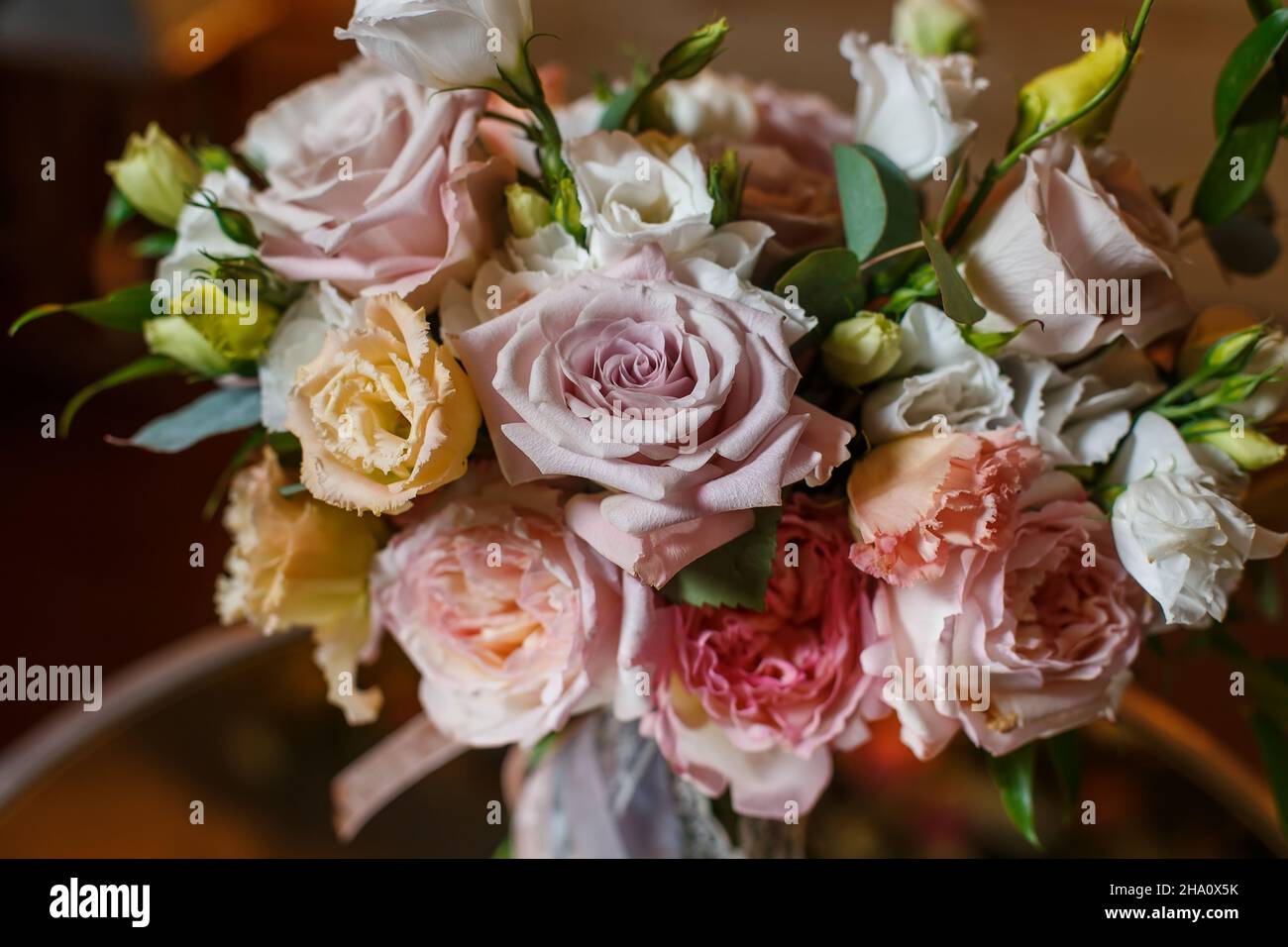 Zarte und sehr schöne Hochzeit Bouquet von Rosen, Grün, eustoma stehend auf Spiegeltisch. Braut trendige Blumen in Pastellfarben auf dem Hintergrund der abendlichen Glühbirnen Stockfoto