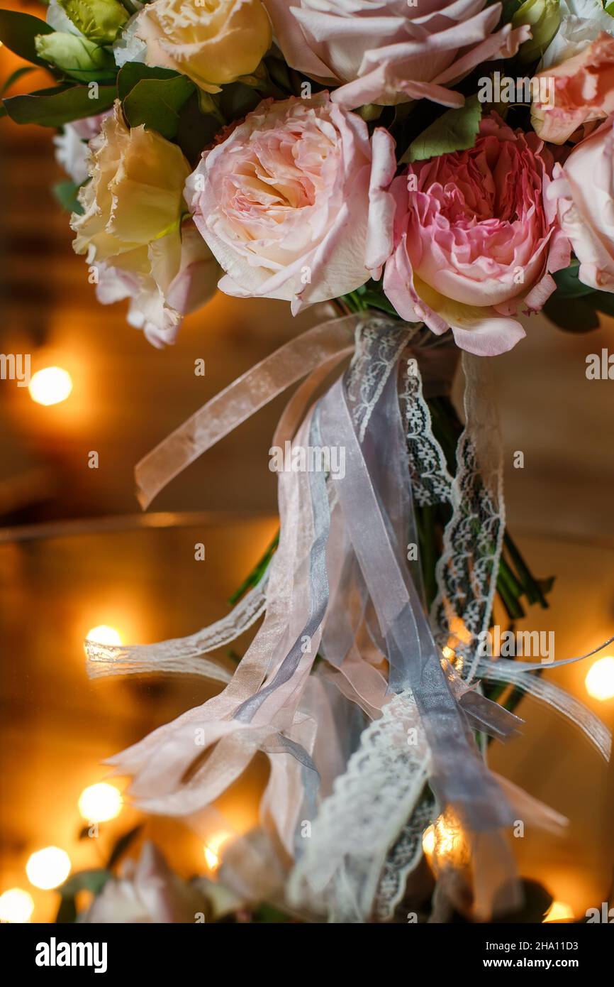 Zarte und sehr schöne Hochzeit Bouquet von Rosen, Grün, eustoma stehend auf Spiegeltisch. Braut trendige Blumen in Pastellfarben auf dem Hintergrund der abendlichen Glühbirnen Stockfoto