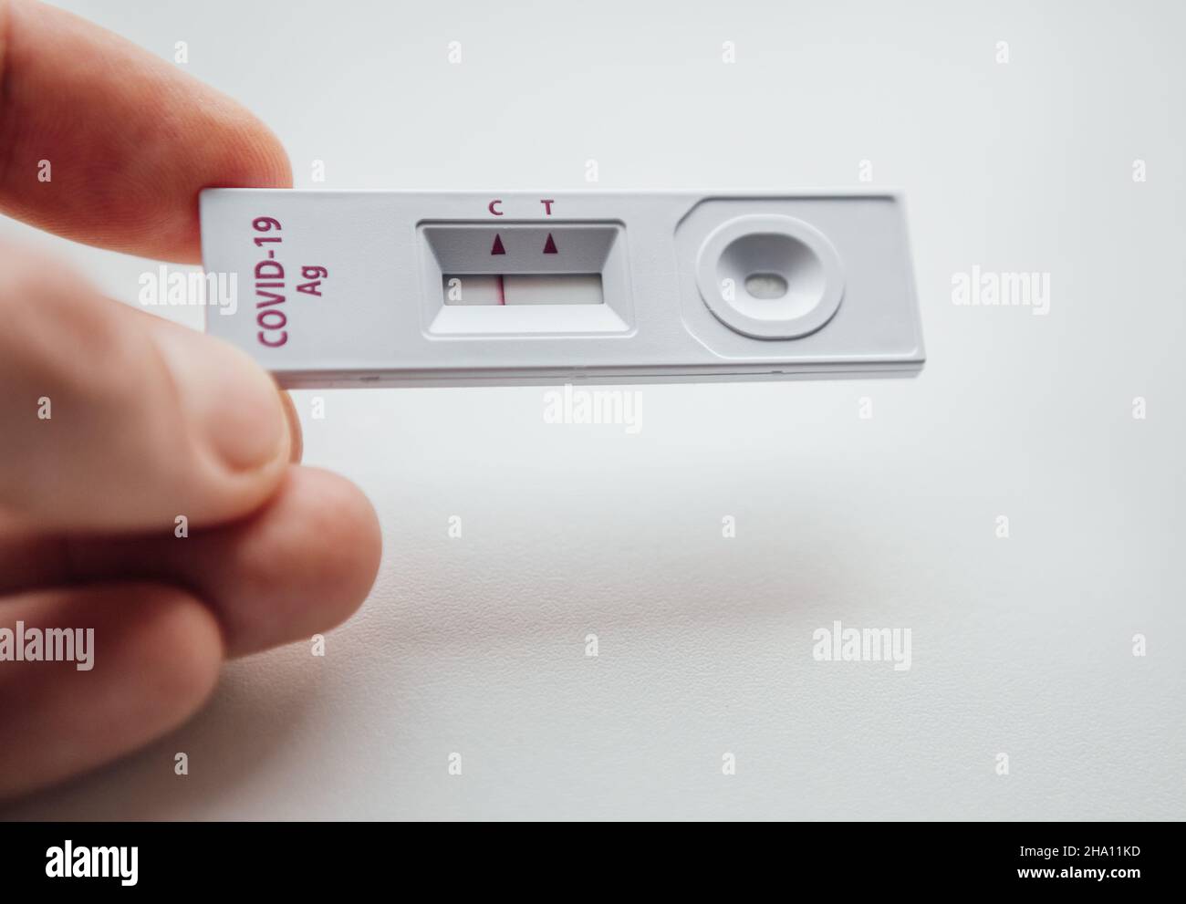 RADT (Rapid Antigen Detection Test) mit einem roten Streifen, der EIN NEGATIVES Ergebnis eines Tests mit menschlicher Probe zeigt. Man-Finger, die den weißen Plastik-de Stockfoto