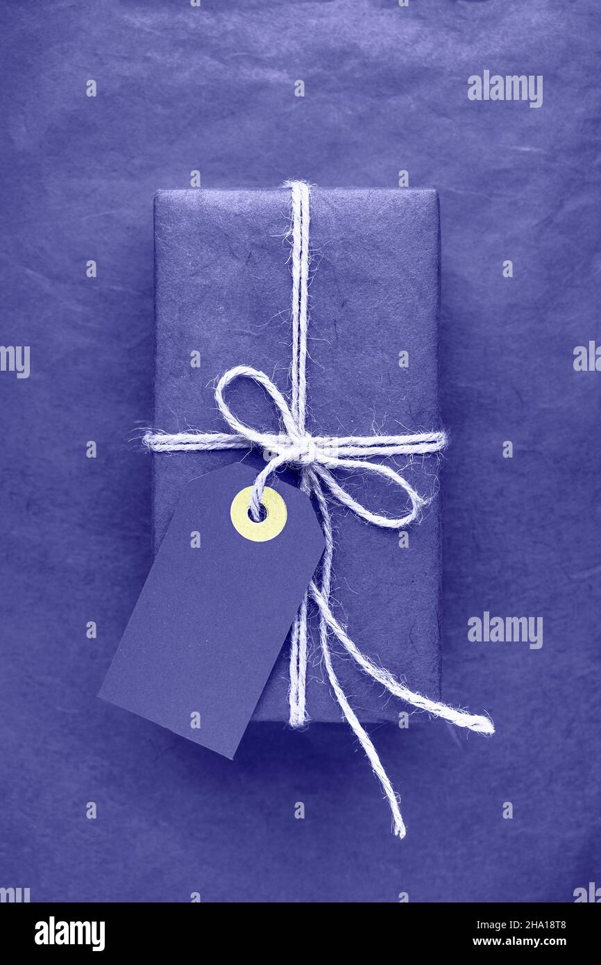 Verpackte Geschenkbox mit Anhänger über lila sehr peri Farbe Hintergrund. Farbe des Jahres 2022 sehr peri getönt. Speicherplatz kopieren Stockfoto