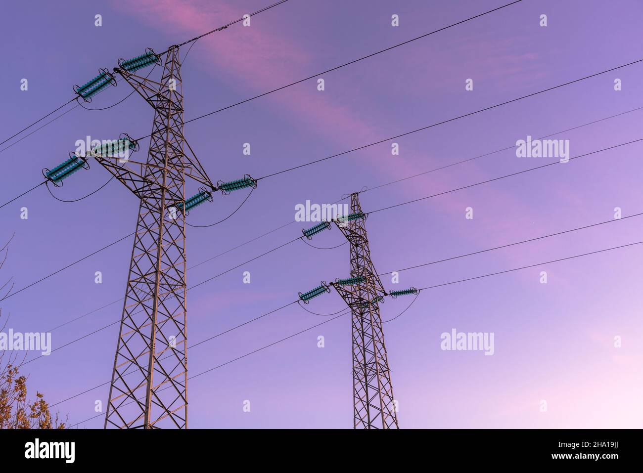 Detail von zwei Strommasten, die Hochspannungskabel in der Abenddämmerung im Winter unterstützen Stockfoto