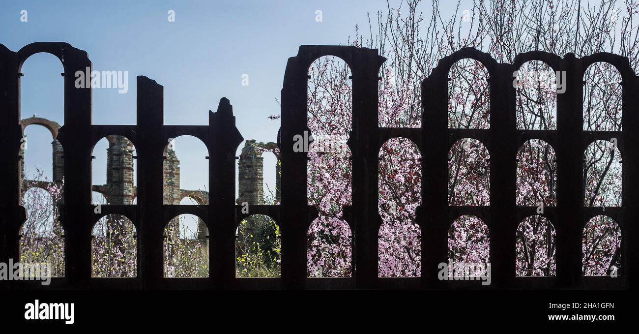 Aquädukt Los Milagros durch eine eiserne Gedenktafel gesehen. Rosa Blüten des Frühlings auf dem Hintergrund Stockfoto