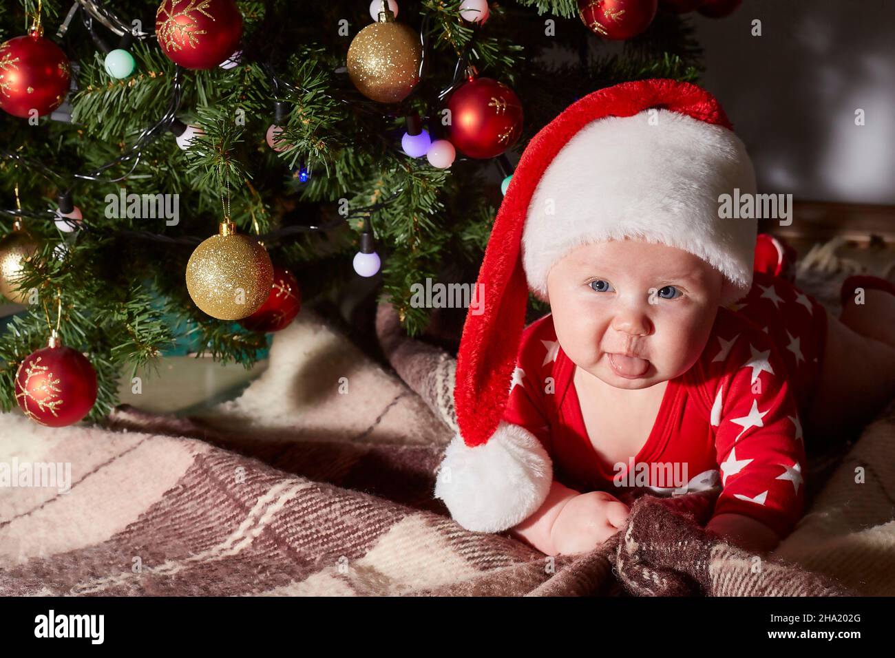 Kaukasisches Baby zeigt seine Zunge und kriecht zu Hause unter dem Weihnachtsbaum. Lifestyle. Copy space. Stockfoto