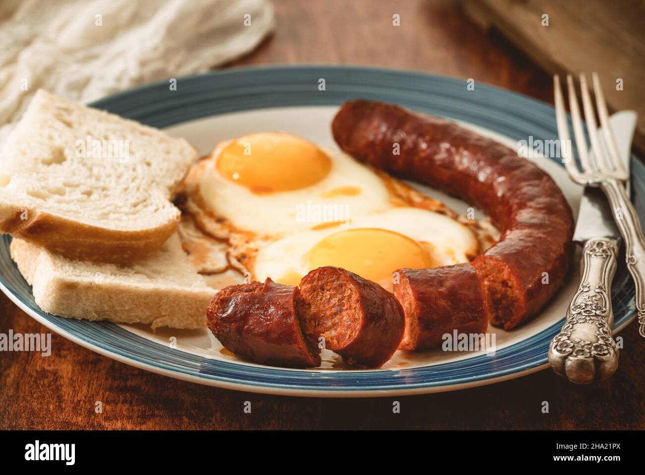 Spiegeleier, Wurst und Brot auf einem Teller aus der Nähe auf Holzhintergrund Stockfoto