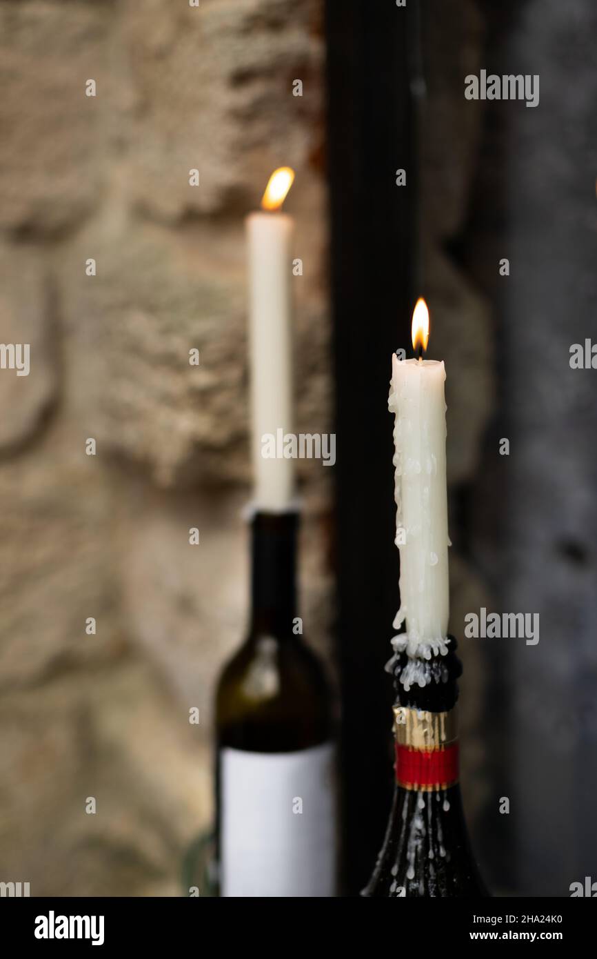 Kerzen brennen in Wein- und Sektflaschen auf der Fensterbank. Vorderansicht. Stockfoto