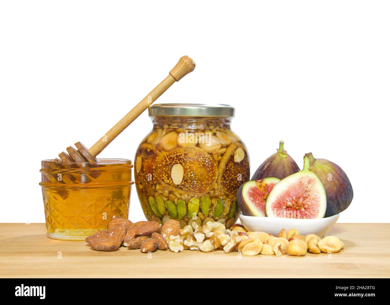 Glas mit Nüssen und Früchten in einem Glas Honig konserviert. Zutaten Pistazien, Walnüsse, Erdnüsse, Mandeln und Feigen auf einem hellen Holztisch isoliert auf Weiß. Stockfoto
