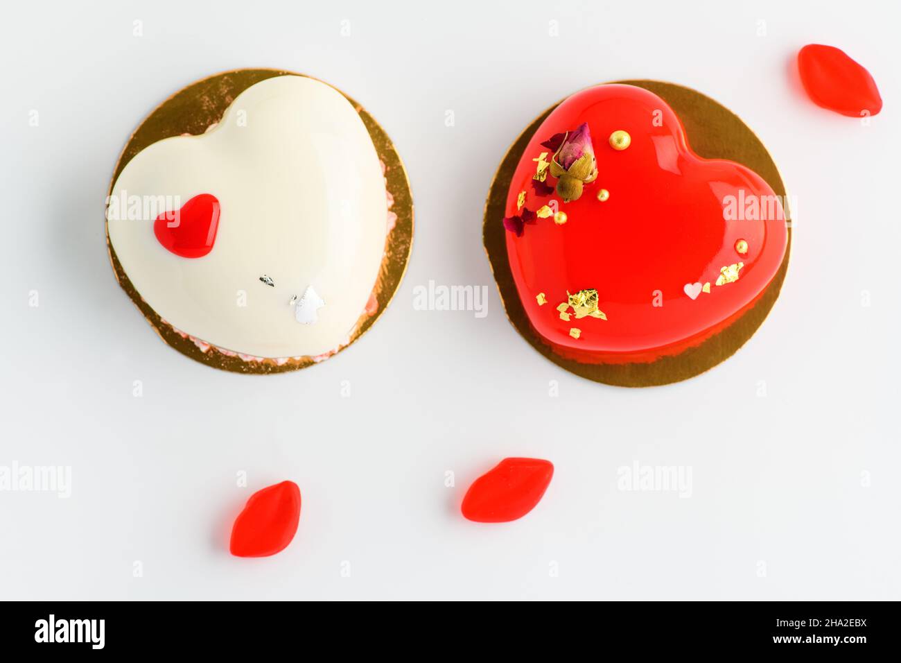 Ein Kuchen in Herzform. Zwei herzförmige Mousse Cupcakes weiß und rot und Süßigkeiten auf weißem Hintergrund. Valentinstag. Stockfoto