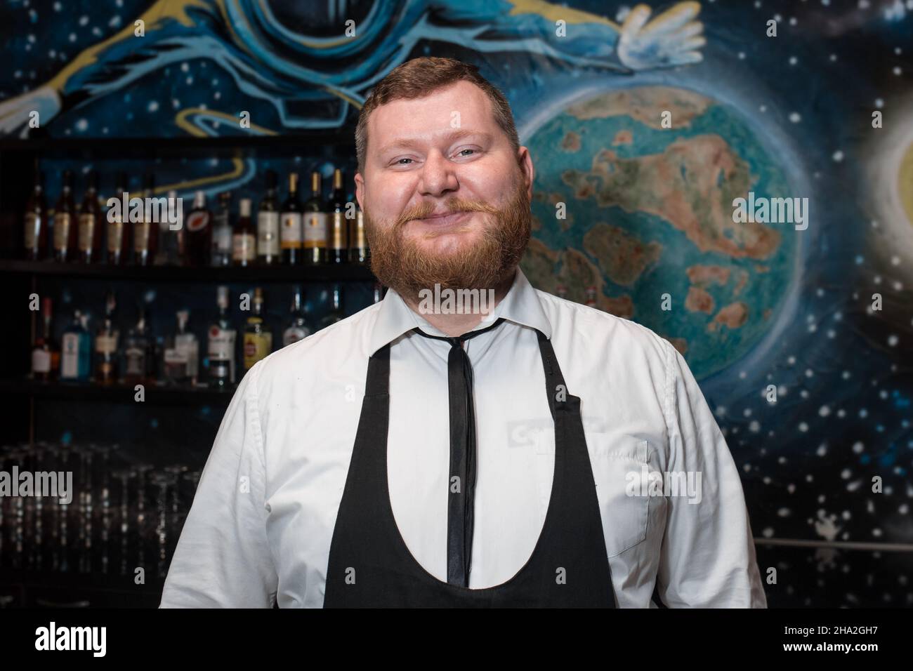 Bärtiger Erwachsener lustig positiv lächelnd kaukasisch aussehend professioneller Barkeeper Portrait im Nachtclub. Stockfoto
