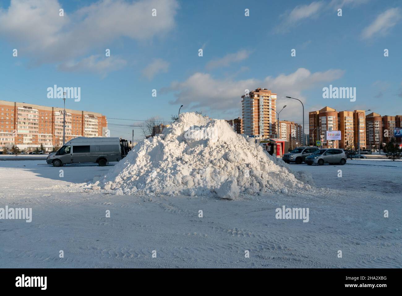 Auf einem Parkplatz auf der Straße liegt nach einem Schneefall ein großer Haufen Schnee mit Wohngebäuden im Hintergrund. Stockfoto