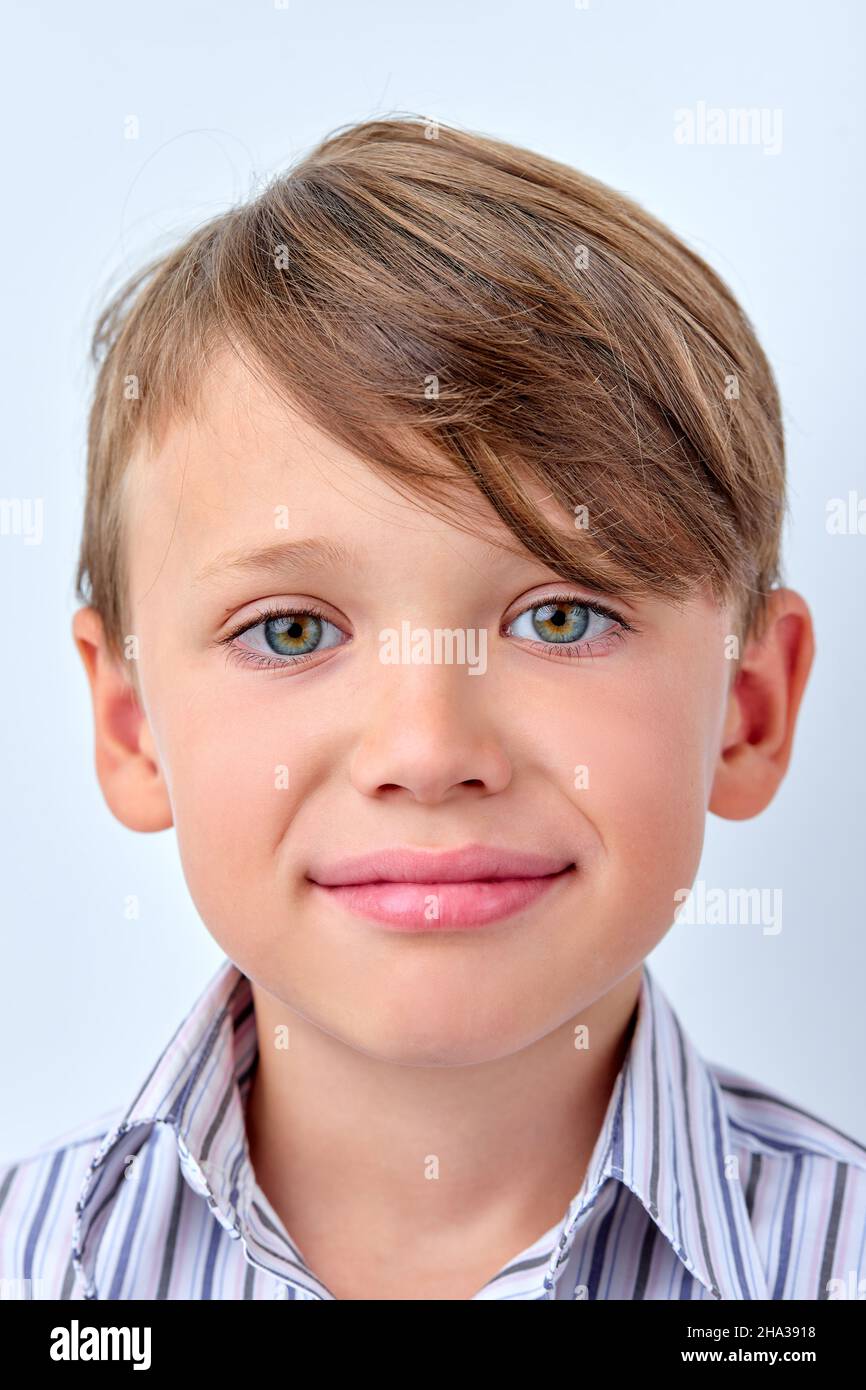 Kleiner Junge verbirgt Unzufriedenheit hinter einem Lächeln, gefälschte menschliche Emotionen Konzept. kaukasisches Kind im Hemd Blick auf die Kamera, mit blauen Augen. Porträt Stockfoto
