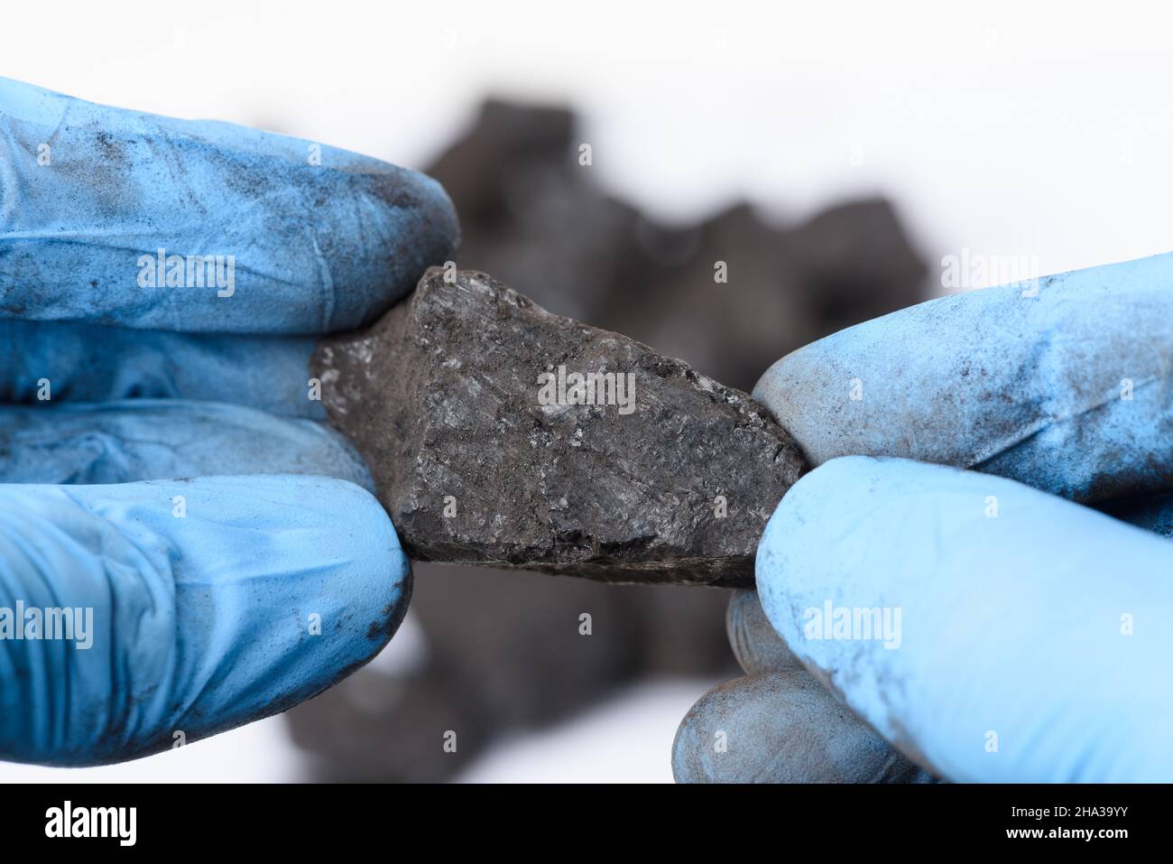 Hände in Handschuhen halten Klumpen schwarzer Kohle im Labor. Forschungskonzept für fossile Brennstoffe. Stockfoto