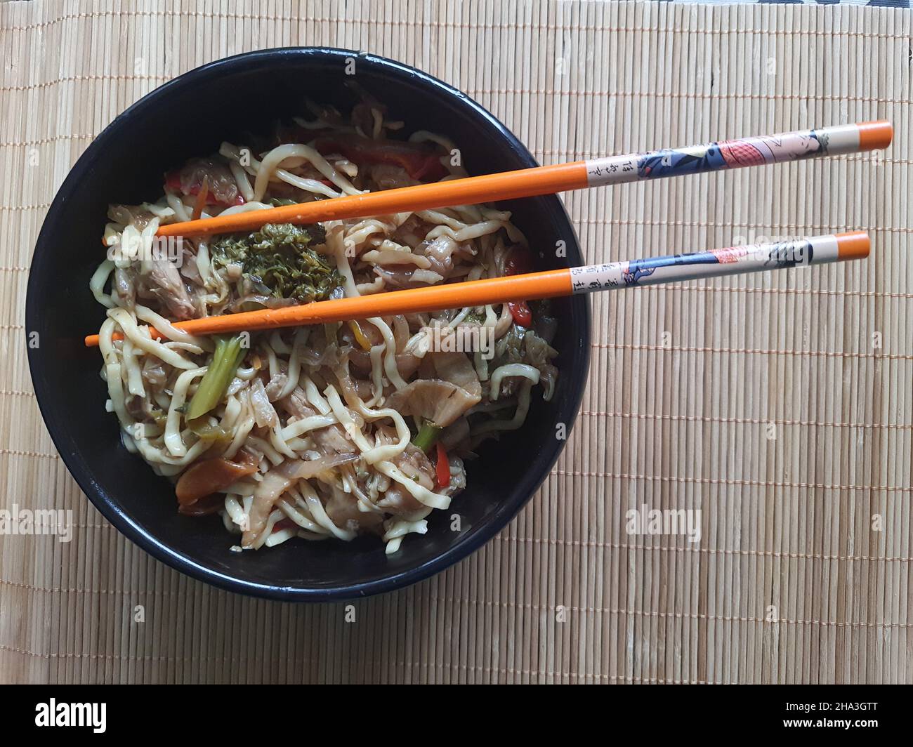 Yakisoba oder Sōsu yakissoba in einer schwarzen Geschirrschüssel mit orientalischem Besteck über einem Bambus-Tischset. Blick von oben. Stockfoto
