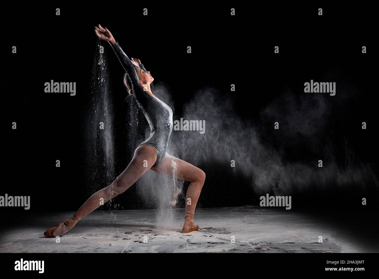 Flexible Balletttänzerin Frau tanzen und streuen Mehl auf schwarzem Hintergrund, attraktive schlanke Dame in schwarzem Body in Zeitlupe, Bewegung GRA Stockfoto